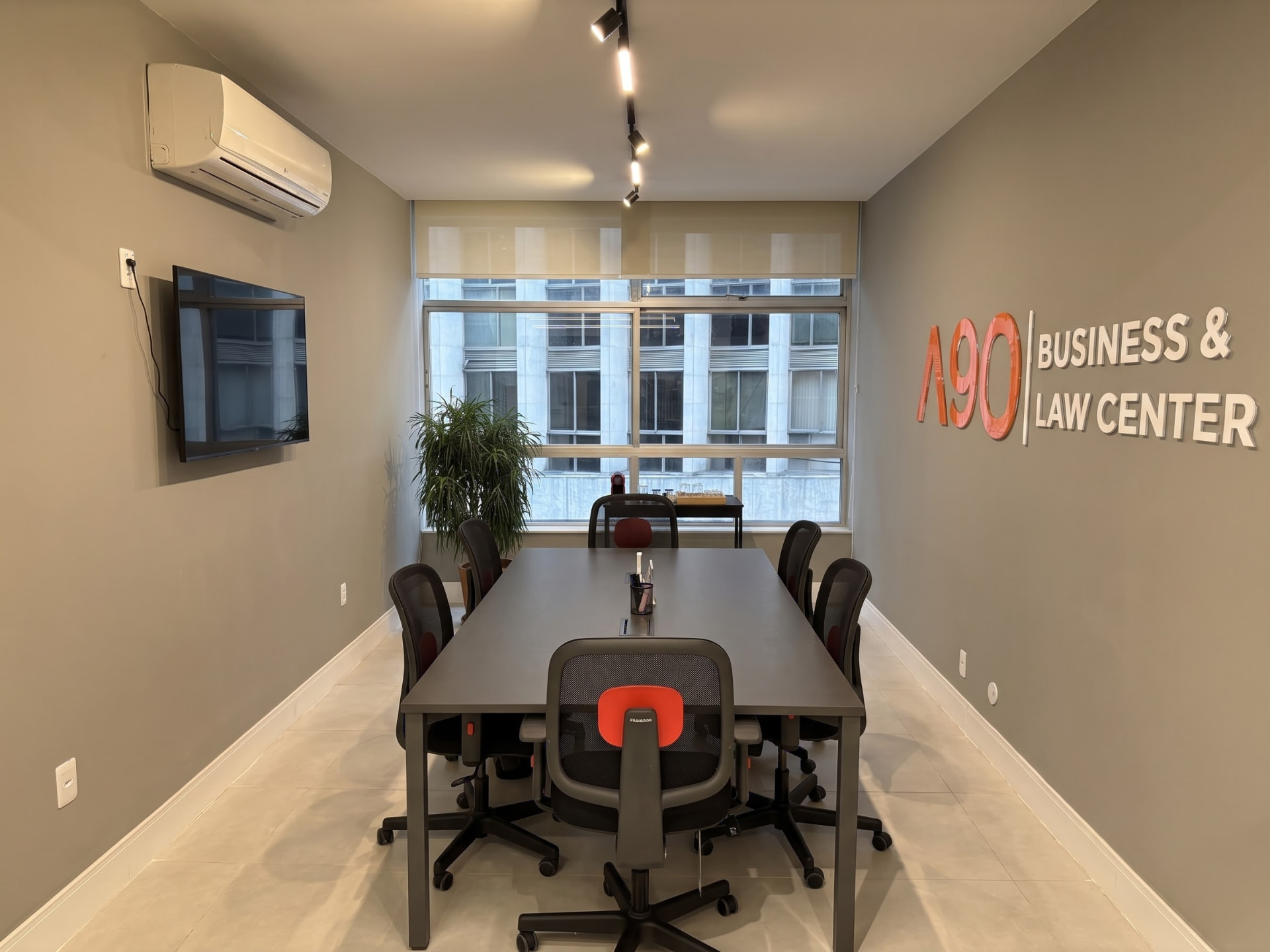 Sala privativa do A90 com mesa de reunião, TV e janela para o Centro do Rio